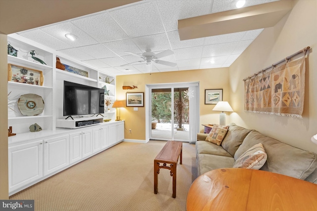 carpeted living room featuring built in shelves, ceiling fan, and a drop ceiling