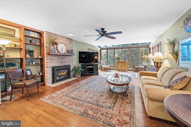 living room featuring a brick fireplace, vaulted ceiling, ceiling fan, and light wood-type flooring