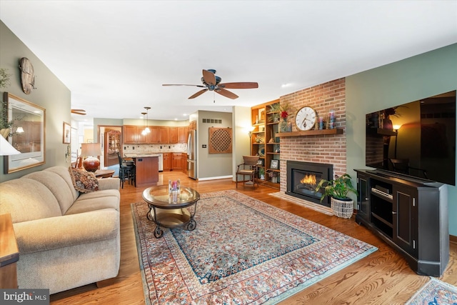 living room with a brick fireplace, light hardwood / wood-style flooring, and ceiling fan