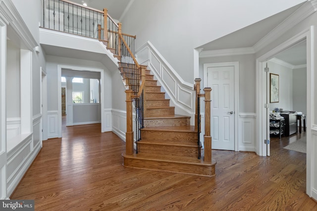 stairs with hardwood / wood-style flooring, a high ceiling, and ornamental molding