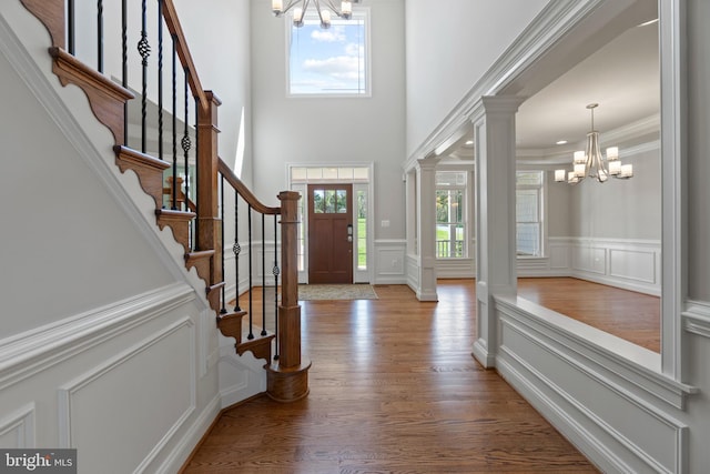 foyer entrance featuring ornate columns, hardwood / wood-style flooring, an inviting chandelier, and ornamental molding