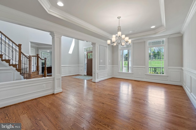 unfurnished dining area with crown molding, light hardwood / wood-style flooring, a tray ceiling, decorative columns, and a chandelier