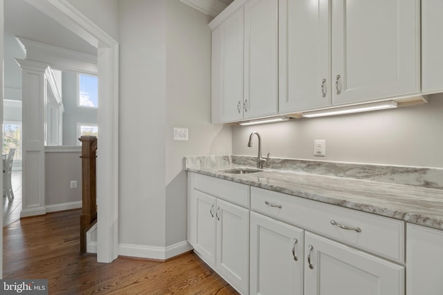 kitchen featuring sink, hardwood / wood-style floors, white cabinetry, and light stone countertops