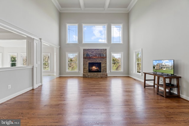 living room featuring a stone fireplace, a healthy amount of sunlight, beamed ceiling, and wood-type flooring