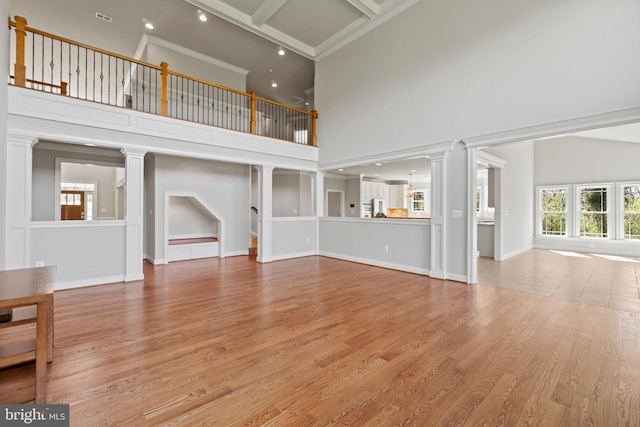 unfurnished living room featuring light wood-type flooring, beam ceiling, a high ceiling, and ornate columns