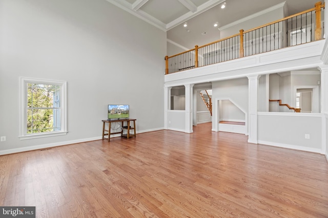 unfurnished living room with light wood-type flooring, a towering ceiling, coffered ceiling, and crown molding