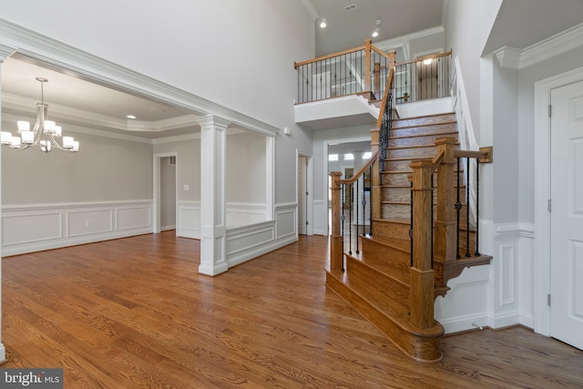 staircase with ornate columns, wood-type flooring, ornamental molding, and a notable chandelier