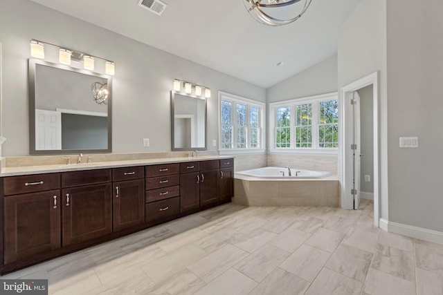 bathroom featuring vanity, tiled bath, and lofted ceiling