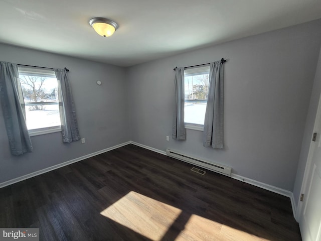 unfurnished room featuring a healthy amount of sunlight, baseboard heating, and dark wood-type flooring