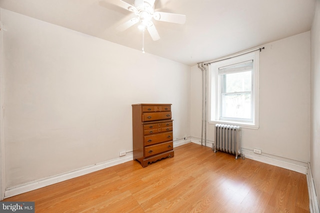 spare room featuring ceiling fan, radiator heating unit, and light wood-type flooring