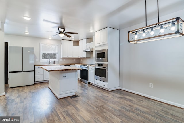 kitchen featuring under cabinet range hood, wood finished floors, wooden counters, and stainless steel appliances