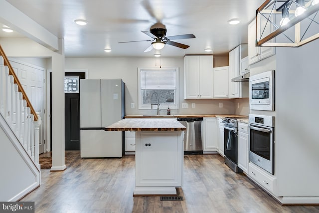 kitchen with wooden counters, a sink, stainless steel appliances, under cabinet range hood, and a center island