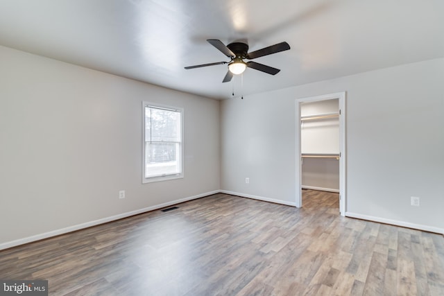 unfurnished bedroom featuring ceiling fan, a walk in closet, a closet, and light wood-type flooring