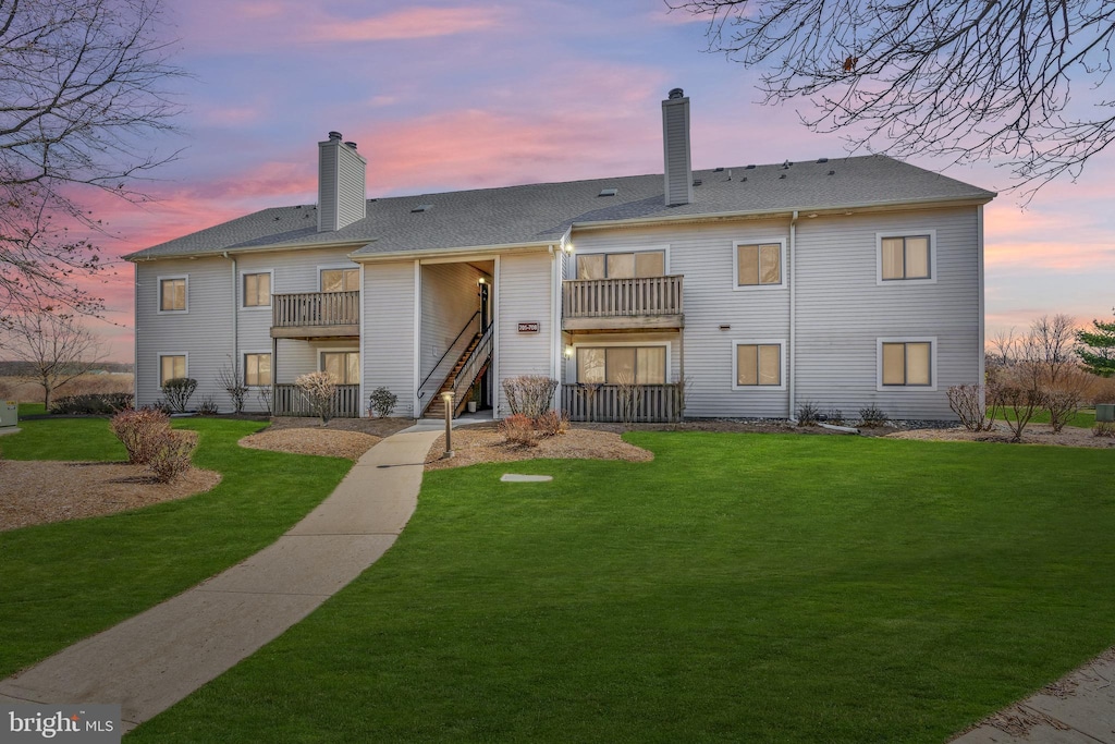 back house at dusk featuring a balcony and a lawn