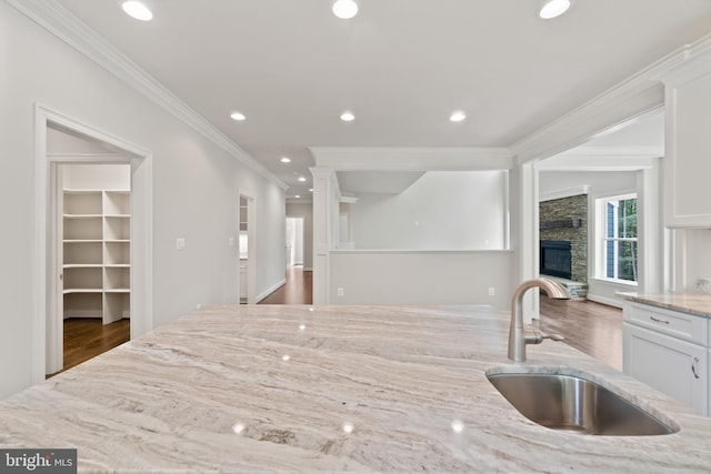 kitchen with crown molding, sink, white cabinetry, a stone fireplace, and light stone counters