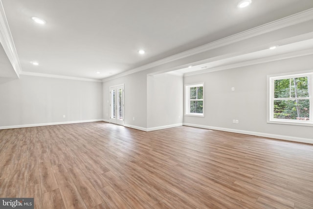 empty room featuring a wealth of natural light, ornamental molding, and light wood-type flooring