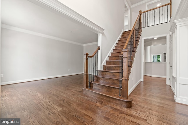 stairs with hardwood / wood-style flooring, ornamental molding, and a towering ceiling