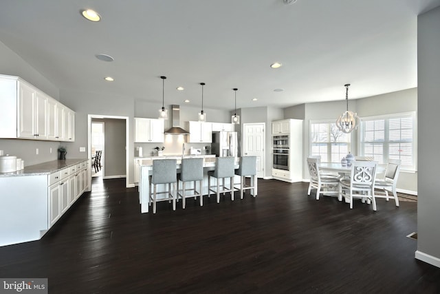 kitchen featuring pendant lighting, white cabinetry, wall chimney range hood, and stainless steel appliances