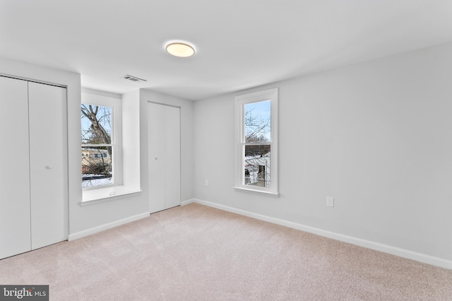 unfurnished bedroom with light colored carpet and two closets