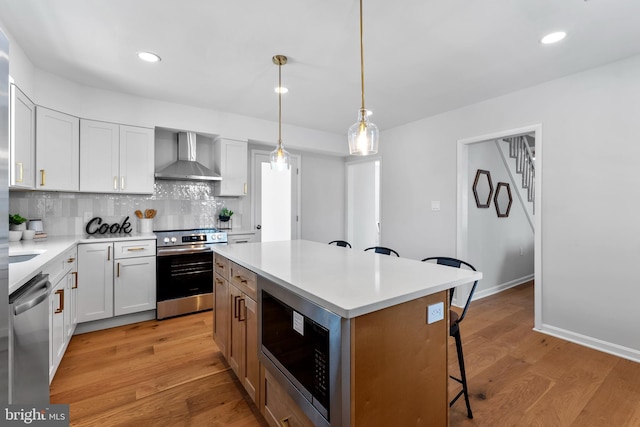 kitchen with wall chimney range hood, a kitchen island, white cabinets, and appliances with stainless steel finishes