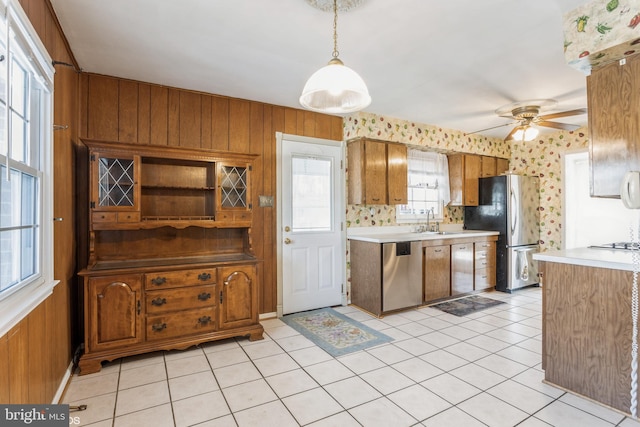 kitchen with appliances with stainless steel finishes, wood walls, sink, hanging light fixtures, and light tile patterned floors