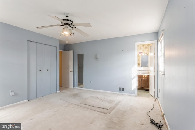 unfurnished bedroom featuring ceiling fan, ensuite bath, a closet, and light carpet