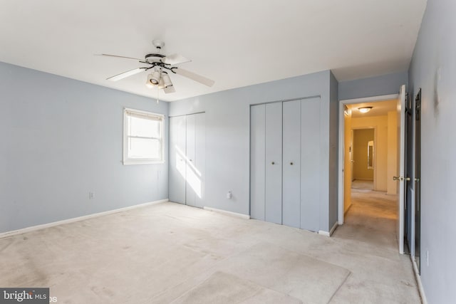 unfurnished bedroom with two closets, light carpet, and ceiling fan