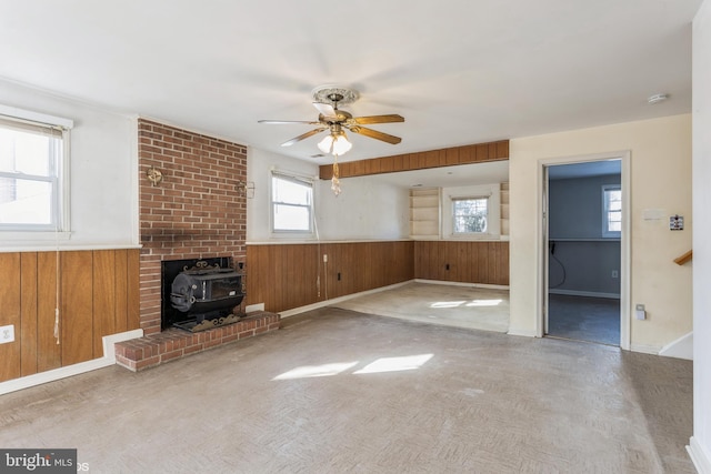 unfurnished living room featuring ceiling fan, a wood stove, and wood walls