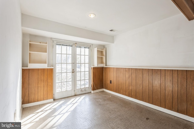 empty room featuring french doors, parquet floors, and wood walls