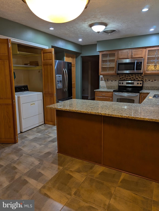 kitchen featuring washer / clothes dryer, light stone countertops, a textured ceiling, and appliances with stainless steel finishes