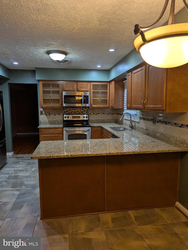 kitchen with sink, appliances with stainless steel finishes, light stone counters, a textured ceiling, and kitchen peninsula