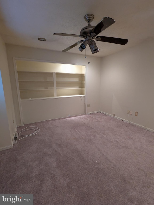 spare room with built in shelves, carpet floors, and ceiling fan