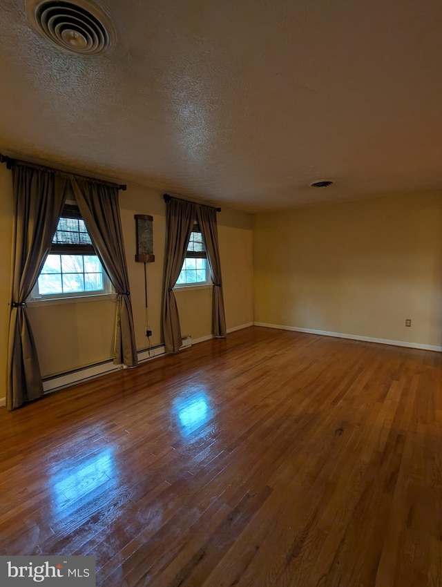 empty room with wood-type flooring, a baseboard radiator, and a textured ceiling