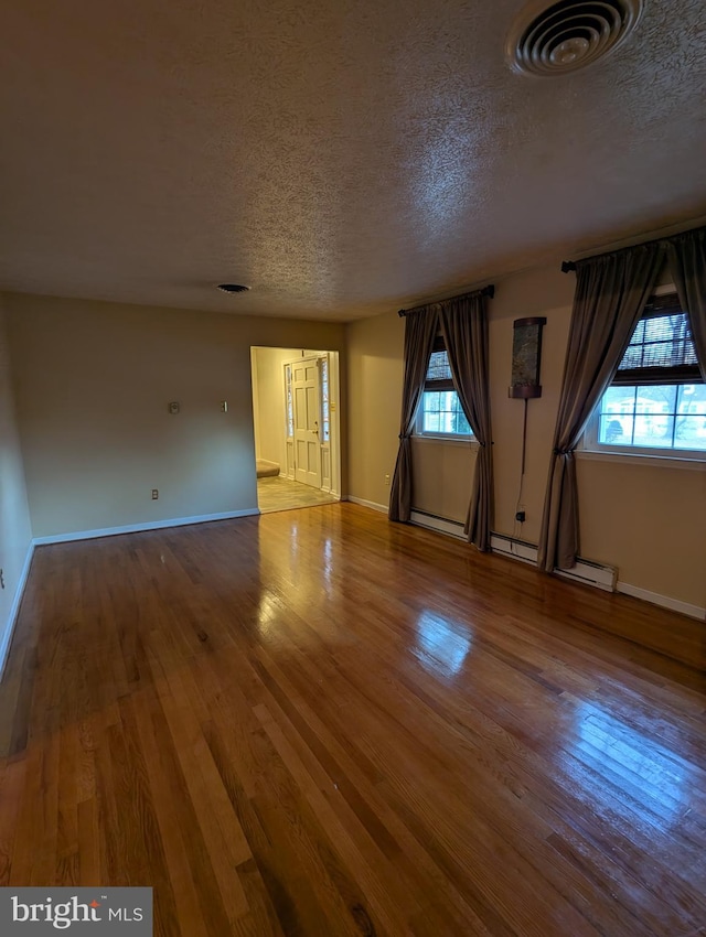 empty room featuring hardwood / wood-style flooring, a baseboard radiator, and a textured ceiling