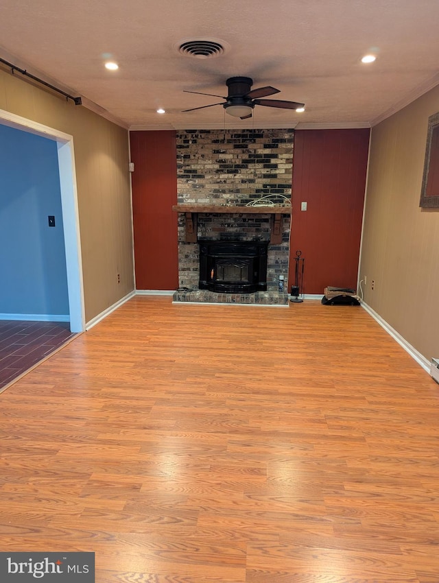 unfurnished living room featuring a large fireplace, ceiling fan, crown molding, a barn door, and light wood-type flooring