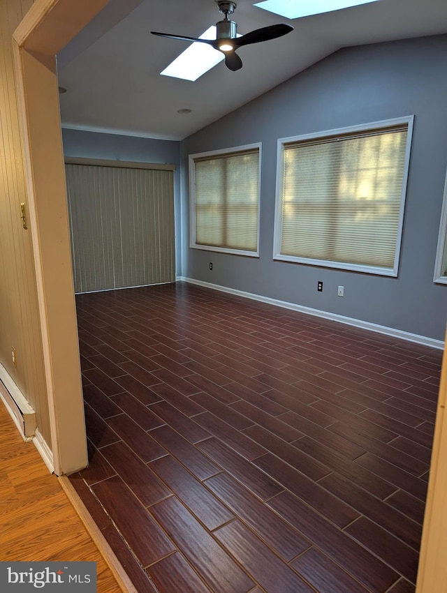 unfurnished room featuring a baseboard heating unit, dark wood-type flooring, vaulted ceiling with skylight, and ceiling fan