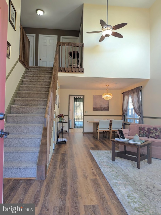 stairs with a towering ceiling, ceiling fan with notable chandelier, and wood-type flooring