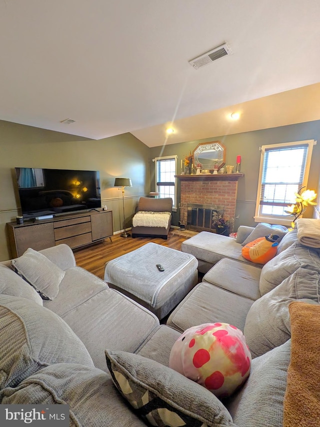 living room with a brick fireplace, a wealth of natural light, and hardwood / wood-style flooring