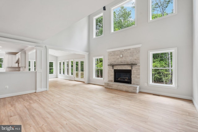 unfurnished living room featuring light wood-type flooring, a towering ceiling, and a stone fireplace