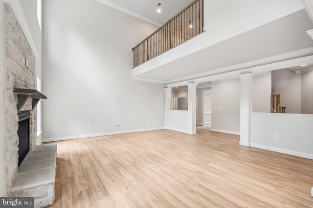 unfurnished living room featuring decorative columns, light hardwood / wood-style floors, a towering ceiling, and a stone fireplace