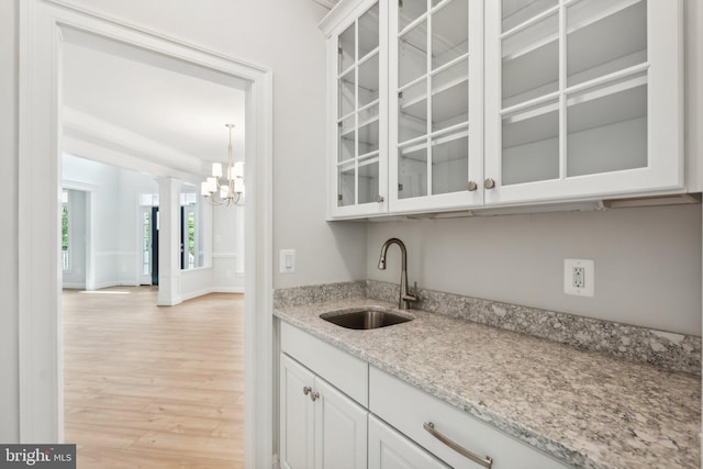 bar with light stone countertops, light hardwood / wood-style floors, white cabinetry, sink, and decorative light fixtures