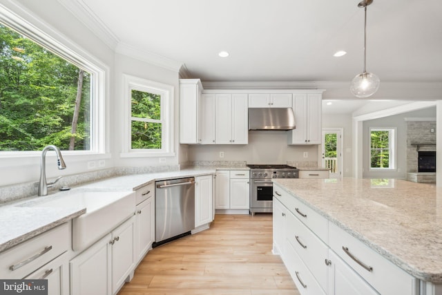 kitchen featuring a stone fireplace, appliances with stainless steel finishes, hanging light fixtures, white cabinets, and light stone counters