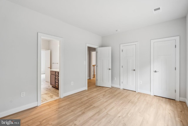 unfurnished bedroom featuring ensuite bathroom, light hardwood / wood-style flooring, and multiple closets