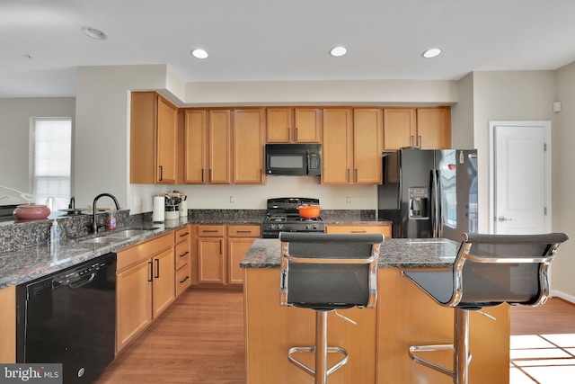 kitchen featuring light hardwood / wood-style flooring, sink, dark stone countertops, black appliances, and a breakfast bar area