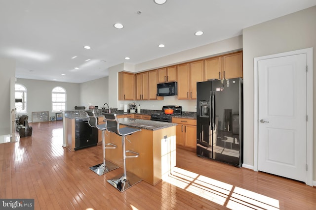 kitchen with a center island, black appliances, dark stone counters, a kitchen breakfast bar, and kitchen peninsula