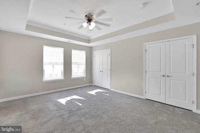 unfurnished bedroom with ceiling fan, two closets, and a raised ceiling