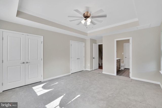 unfurnished bedroom with ceiling fan, ensuite bathroom, a raised ceiling, and light carpet