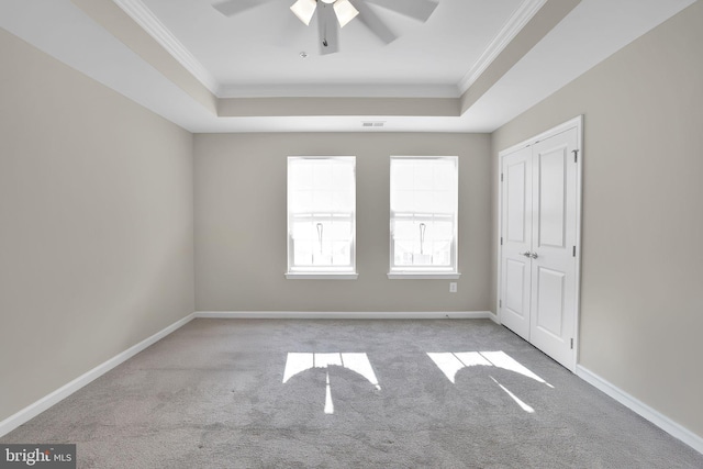 unfurnished room with ceiling fan, light colored carpet, and a tray ceiling