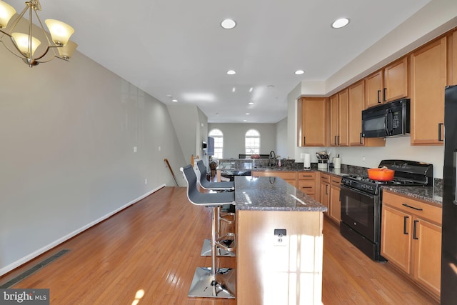 kitchen featuring black appliances, a kitchen bar, dark stone countertops, a kitchen island, and decorative light fixtures