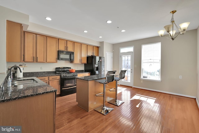 kitchen featuring black appliances, a center island, sink, decorative light fixtures, and dark stone countertops